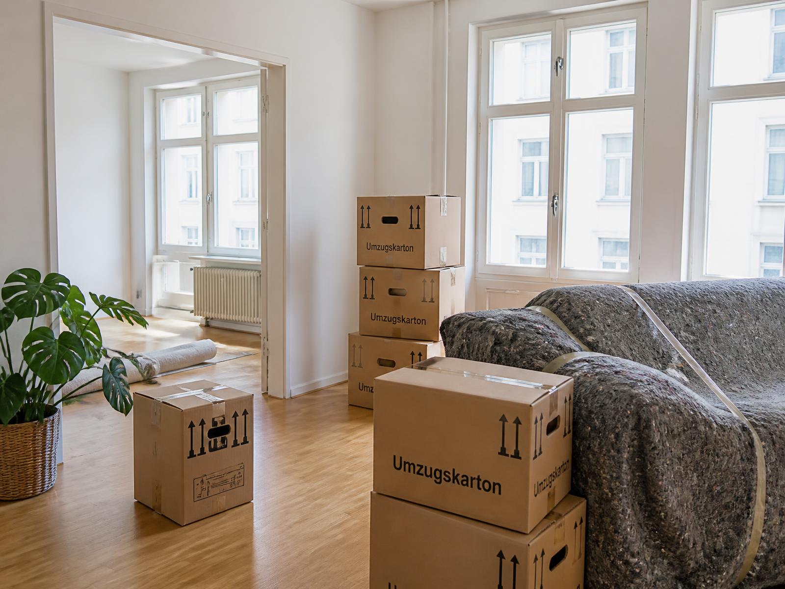 Helle Münchner Wohnung mit gestapelten Umzugskartons und einem in Schutzdecken verpackten Sofa